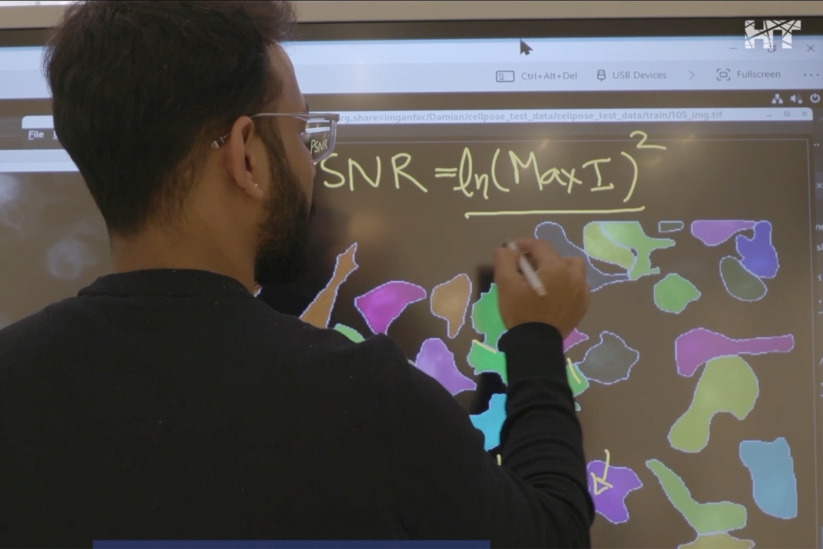 An HT researcher writing the SNR formula next to AI-generated cell segmentation on a large interactive screen